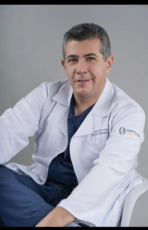 El Dr. Edmundo Escoto sonriendo, con bata blanca y uniforme azul